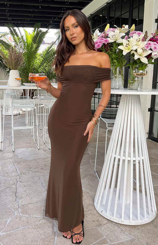 Brunette model wearing brown strapless maxi dress holding a drink at a venue.