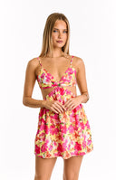 Yellow mini dress with a vibrant pink and orange floral print, featuring a sweet-heart neckline with a twisted front, thin spaghetti straps, and side cut-outs at the waist. A delicate four-leaf clover necklace and a bracelet are worn.