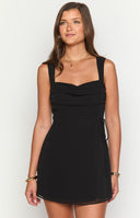 Brunette model wearing a black chiffon mini dress and gold jewellery holding a drink.