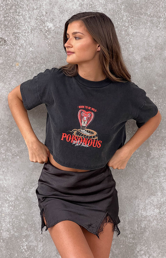 Brunette model wearing a black acid wash cropped graphic tee and a satin mini skirt