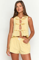 a blonde model with sunglasses wears a yellow gingham top with bows and matching boxer shorts holding a coffee cup