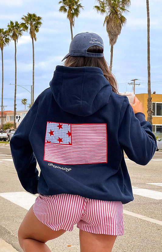 Girl wearing a navy sweatshirt with a red and blue embroidered flag on the back, paired with red and white striped shorts