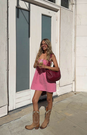 model is wearing a red gingham strapless mini dress paired with cowboy boots