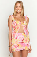 Girl is wearing a chiffon ruffled top with a bright floral print with pinks, yellows, and reds.