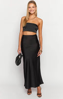 Girl looking away wearing a black maxi skirt and a black strapless top, standing on a balcony.