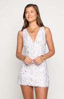 blonde model wearing a lilac floral lace mini dress with gold jewellery and a woven beige bag