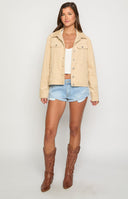 blonde model wearing a cream coloured cord jacket styled for winter with white jeans and a black tank top