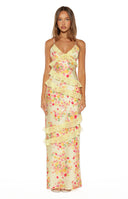 A full-length studio shot of our model wearing a pale yellow maxi dress with a vibrant pink orange and yellow floral print. This maxi dress features thin spaghetti straps a V-neckline and several tiers of sheer diagonal ruffles flowing down the body.
