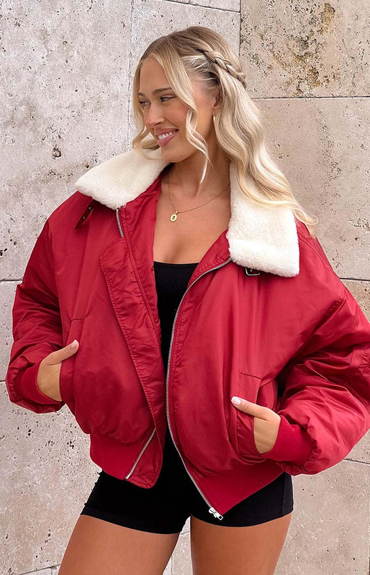 blonde model wearing a red oversized jacket with a faux fur collar over a black playsuit