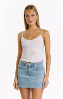 A close-up of a white spaghetti strap top adorned with pink and yellow beaded hibiscus flowers, paired with a light wash denim mini skirt.