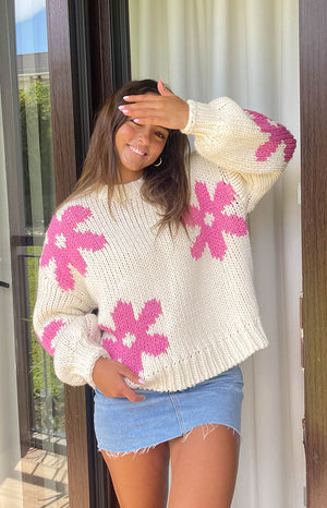 Girl is wearing a thick knit crochet sweater with pink floral designs. She is wearing a blue denim mini skirt.