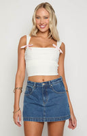 blonde model wearing a mid wash denim mini skort paired with a yellow tank top
