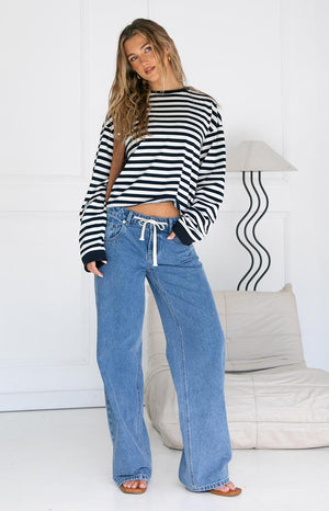 Model wearing a black and white striped long-sleeve top, blue wide-leg jeans with a white drawstring, and brown flat sandals.
