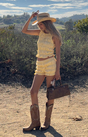 model wearing yellow gingham shorts with ruched and ruffle details and a yellow gingham ruched sleeveless top 