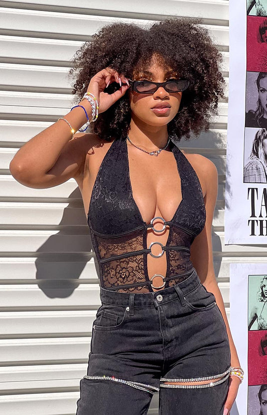 Girl in black lace halter bodysuit and black denim jeans holding a pair of sunglasses.